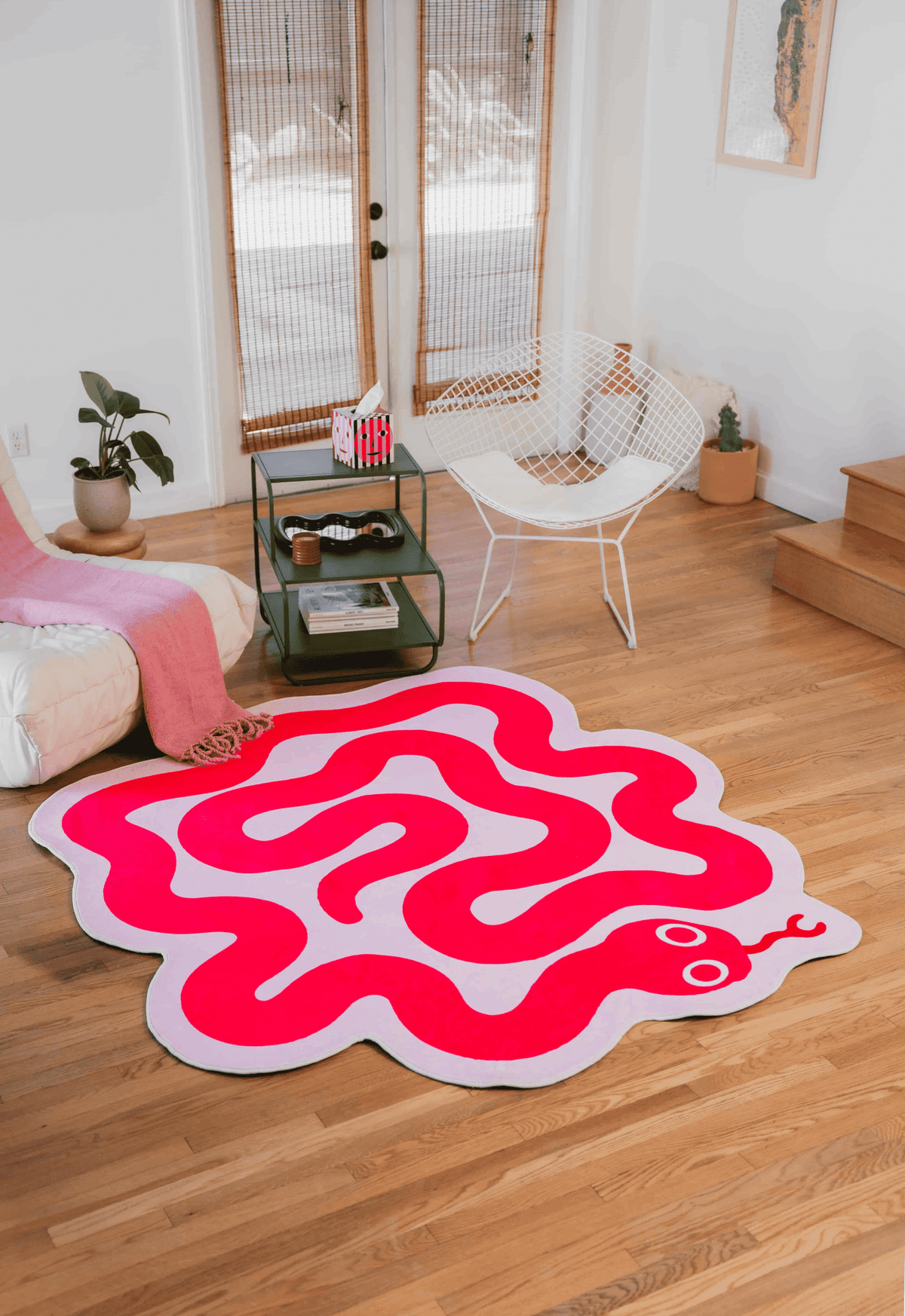 Red and pink snake rug styled in a bright room with wooden floor, a white chair, and green shelving.