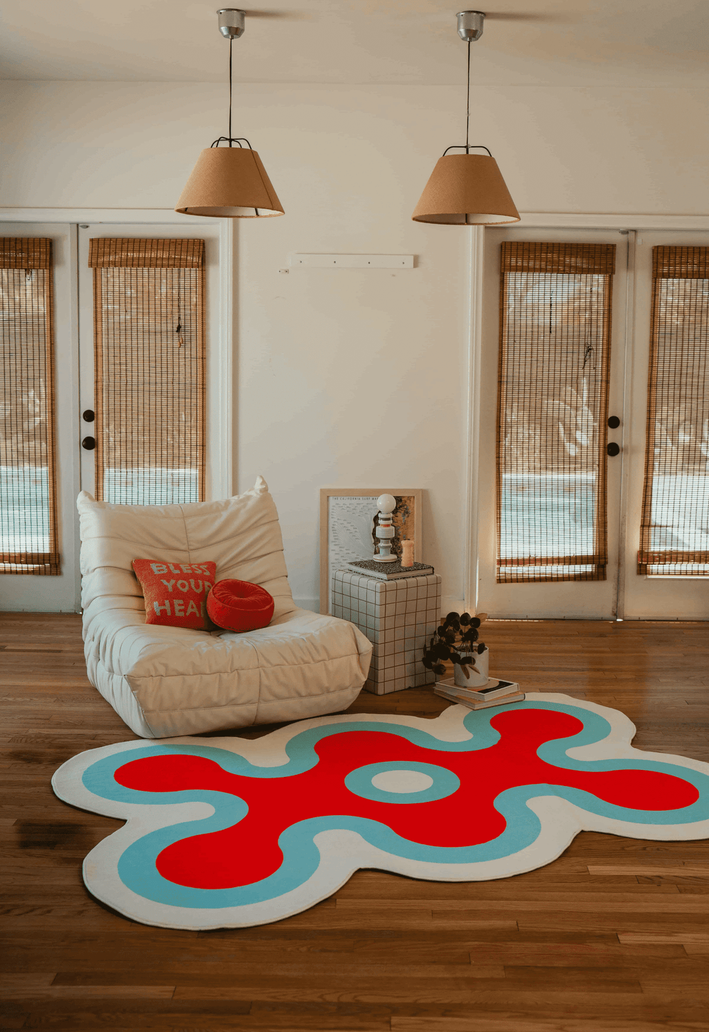 Red and blue irregular coral rug centered in bright room with wood floors, arched doorway, and woven blinds.