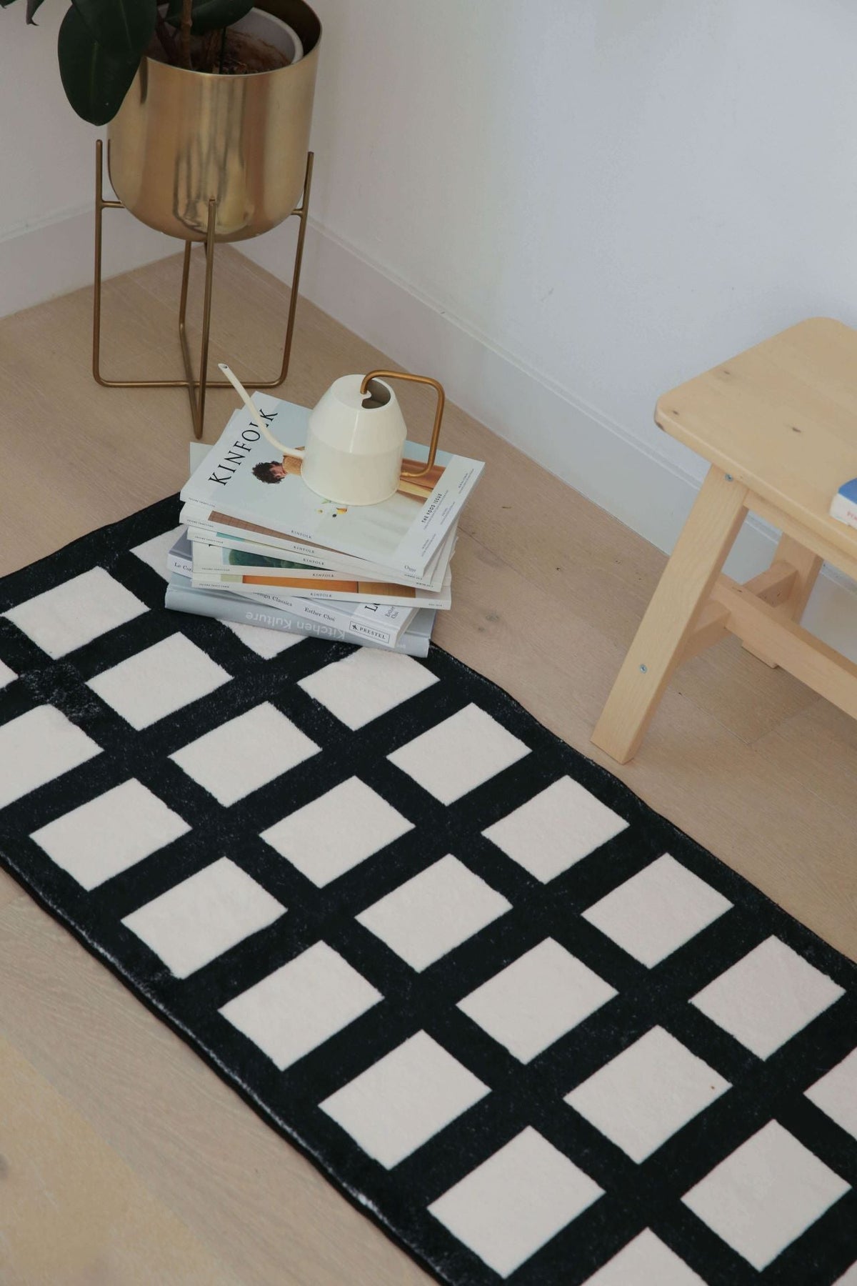 Geometric runner with black and white grid pattern beside a stack of books and a watering can in a cozy corner setup.