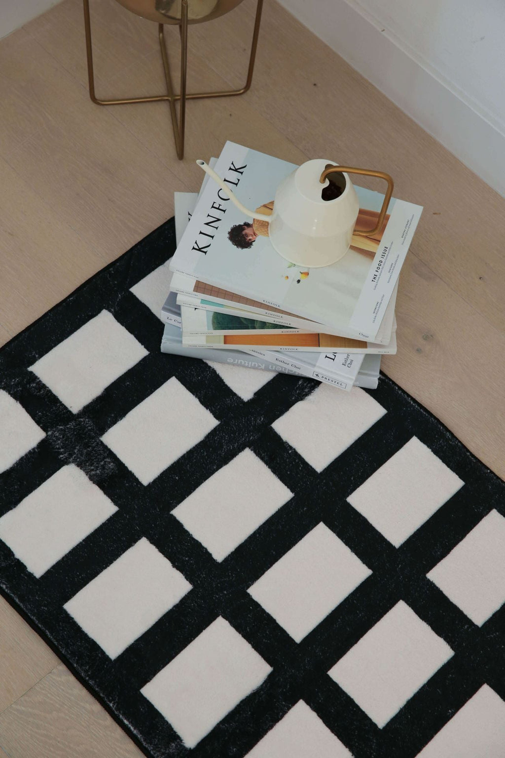 Close-up of the black and white grid runner next to a stack of magazines and a small watering can.