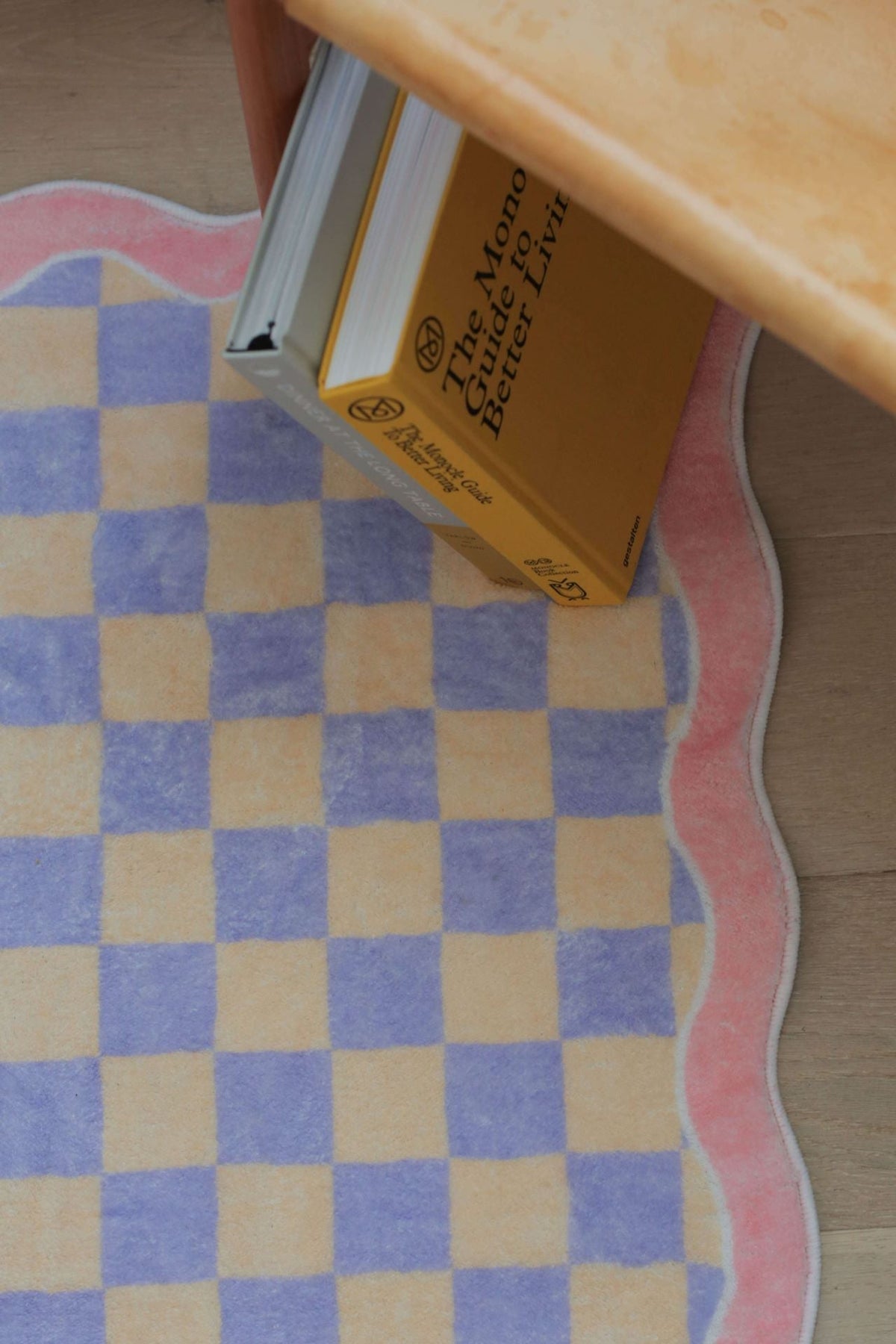 Detail shot of the pastel checkerboard rug, showing the scalloped pink border and books tucked underneath a chair.