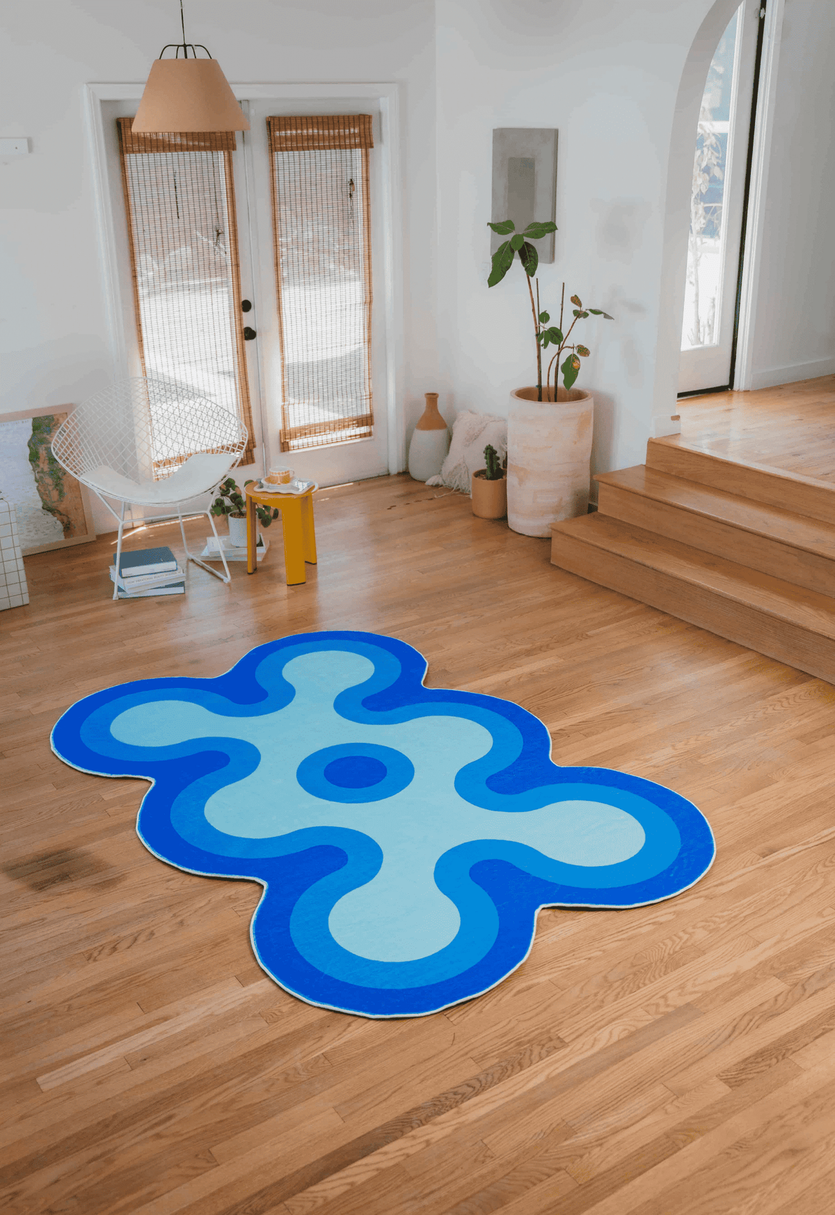 Full view of light blue, blue, and navy irregular coral rug placed in a bright room near stairs and glass doors.
