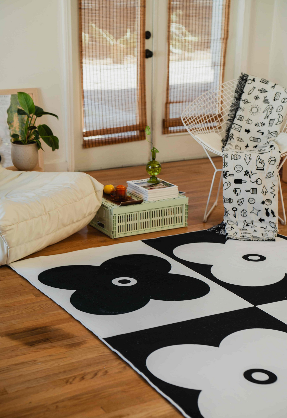 Close-up of black and white floral rug with a modern wire chair and books on a pastel green crate table.