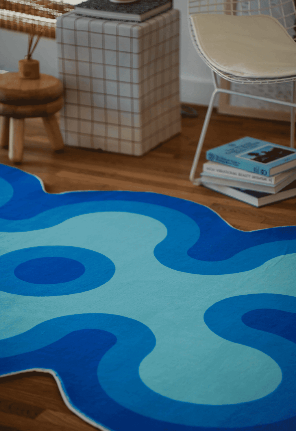 Close-up of irregular coral rug in light blue with dark blue and navy blue accents beside a white chair and checkered side table.