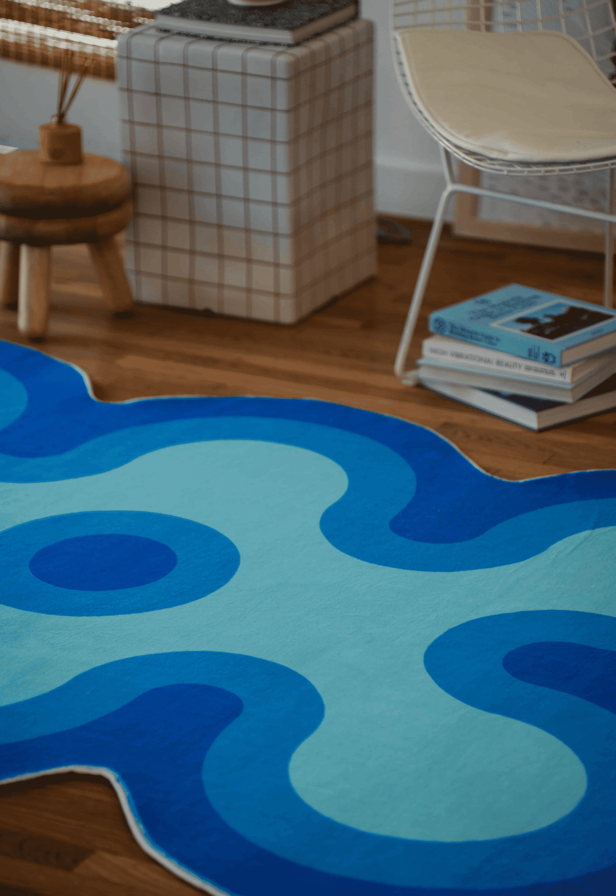 Close-up of irregular coral rug in light blue with dark blue and navy blue accents beside a white chair and checkered side table.