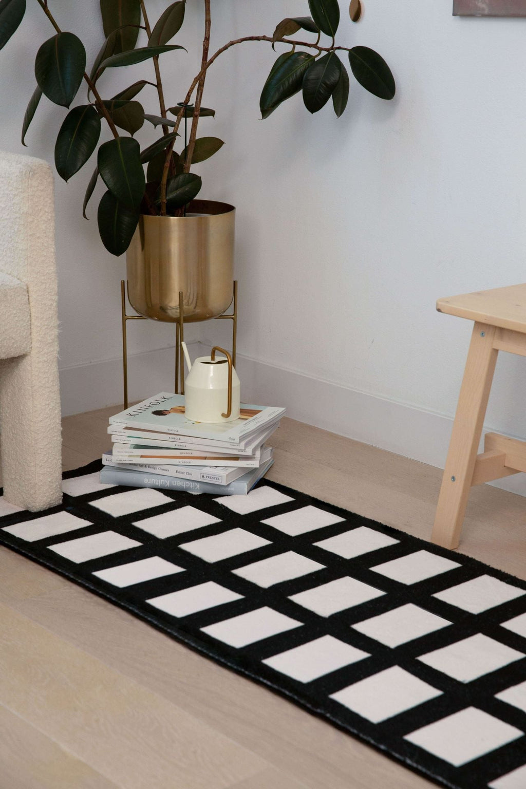 Black and white grid runner styled beside a gold planter and wooden stool in a cozy corner.