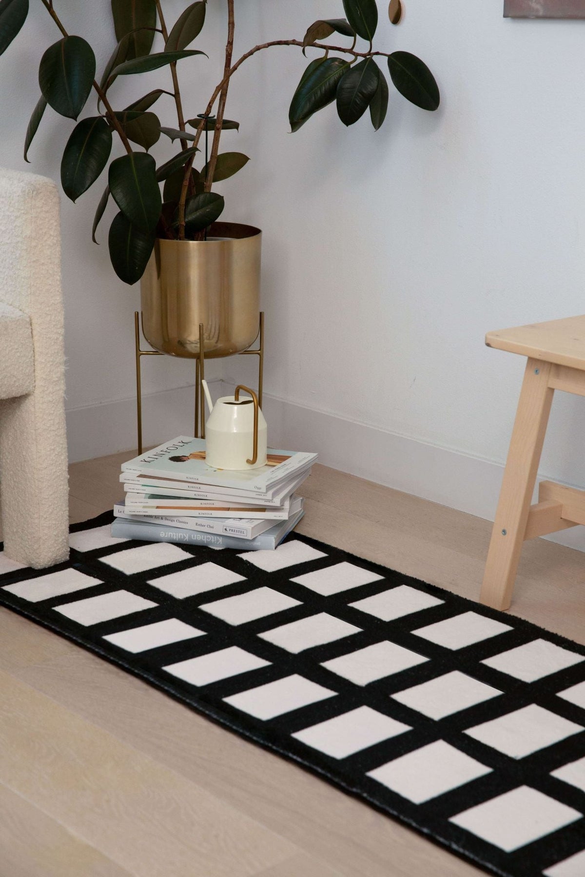 Black and white grid runner styled beside a gold planter and wooden stool in a cozy corner.