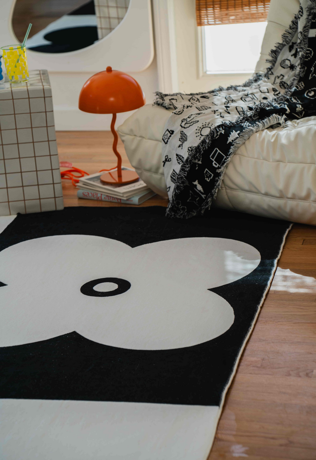Close-up of a black and white flower-patterned rug next to a cream lounge chair and grid side table.