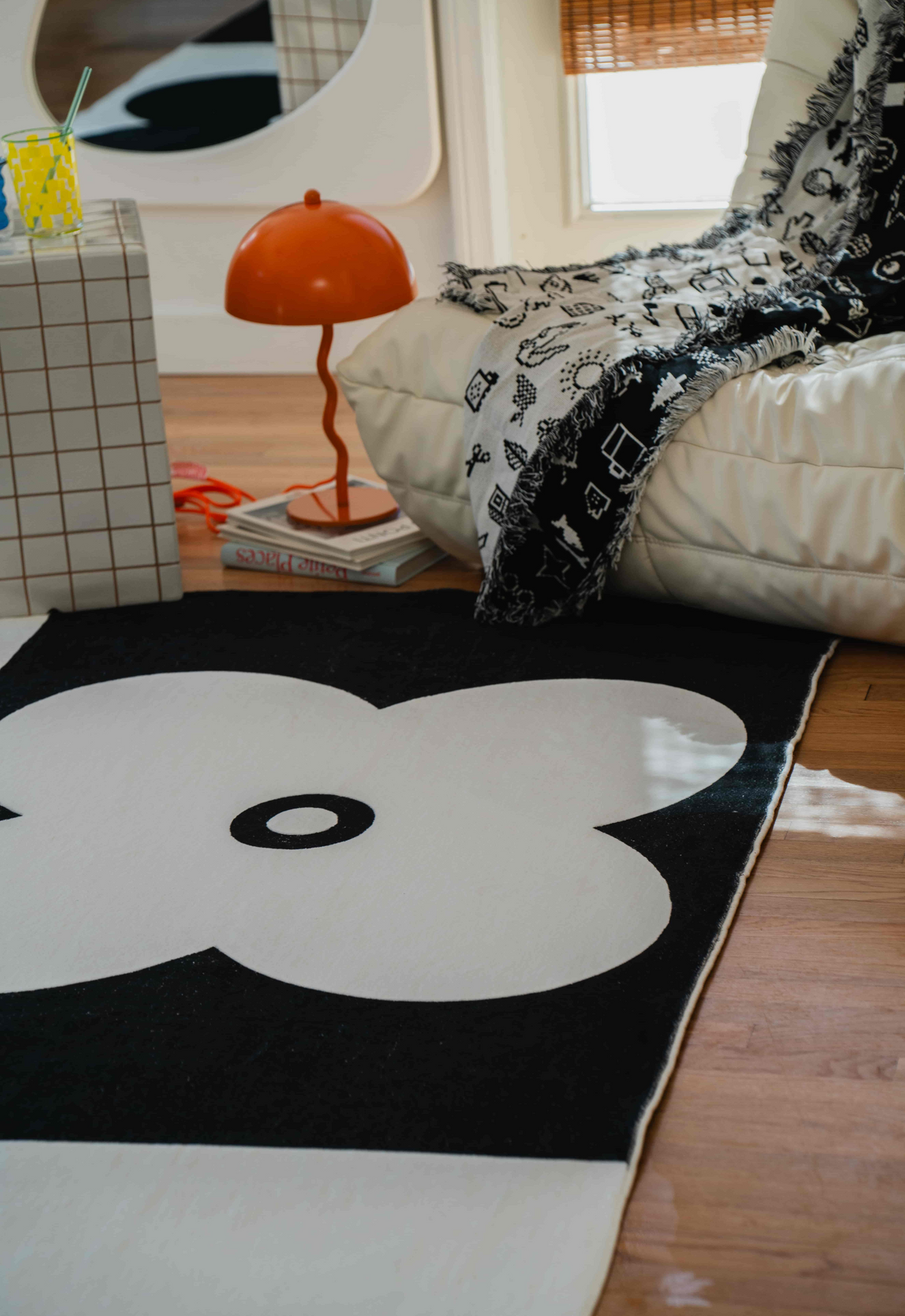 Close-up of a black and white flower-patterned rug next to a cream lounge chair and grid side table.