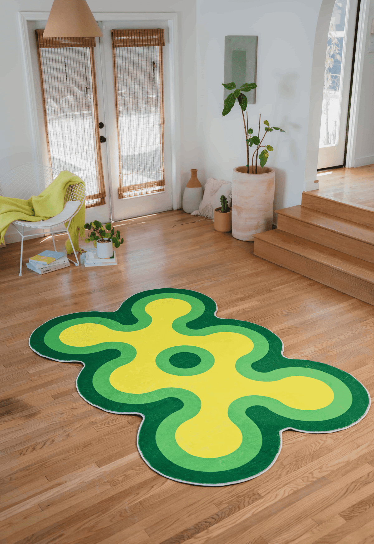 Green and yellow coral-shaped rug laid out in a bright living room with wood floor and minimal decor.