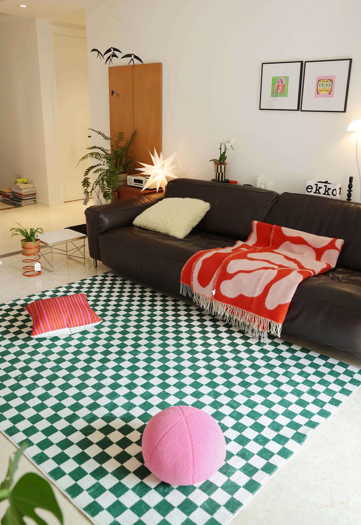 Vibrant Checkered Rug styled with a dark leather sofa, red throw, and playful decor like a pink floor ball and pillow.