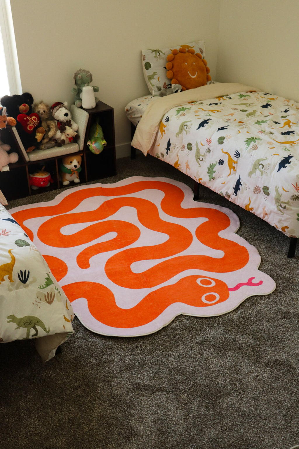 Orange and pink snake rug placed between two kids’ beds with dinosaur-themed bedding.