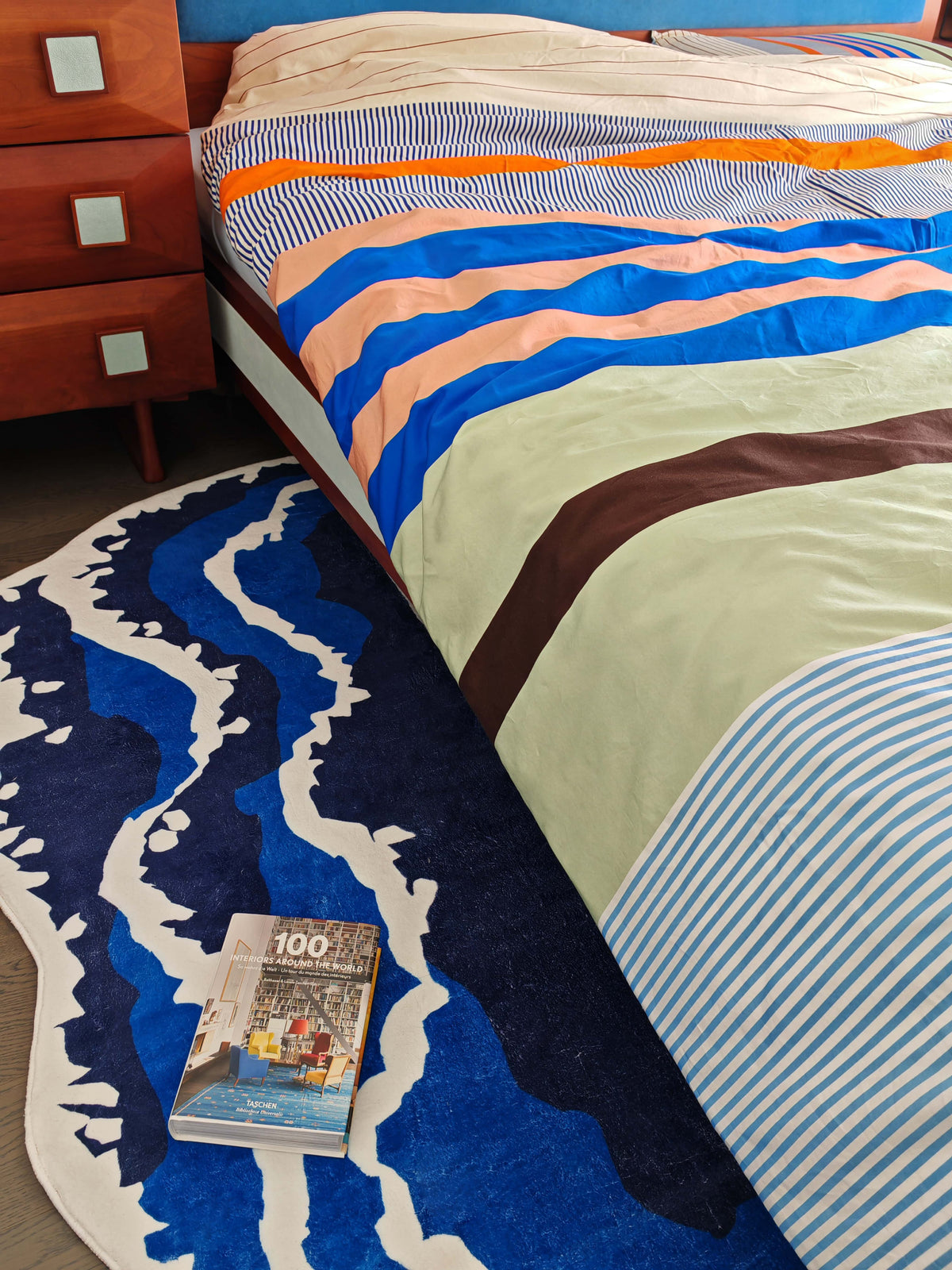 Blue wavy rug by the bed blends with natural tones, bringing a soft organic accent to the relaxed interior.
