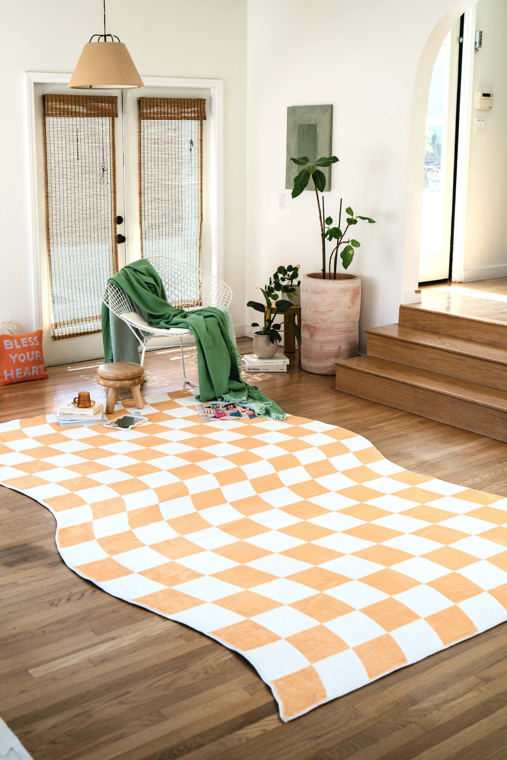 The wavy checkered rug in a bright entryway, paired with a white chair, green throw, and minimal wood decor.