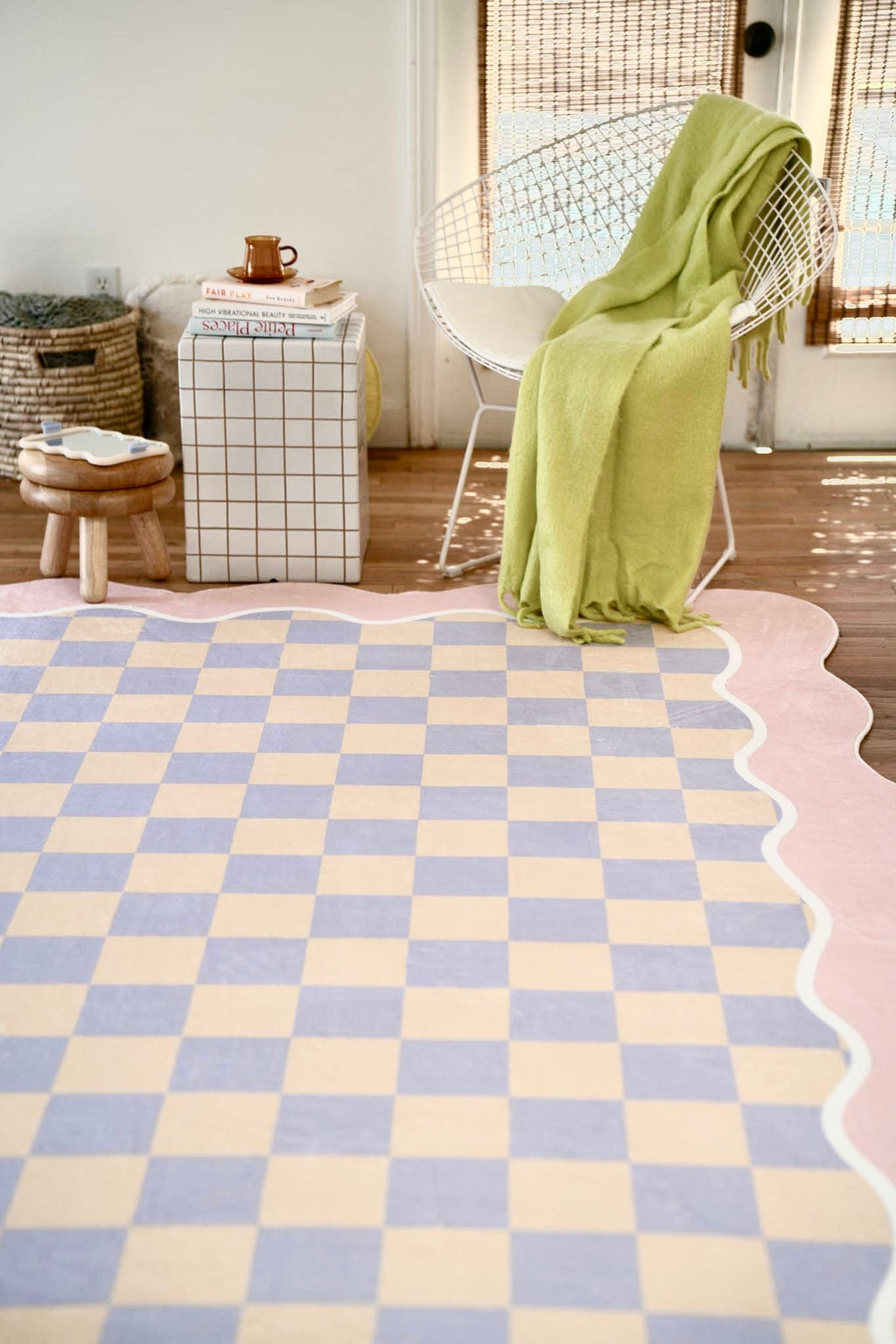 Sunlight spills across the lilac and peach checkered rug, paired with a white armchair and soft-toned surroundings.