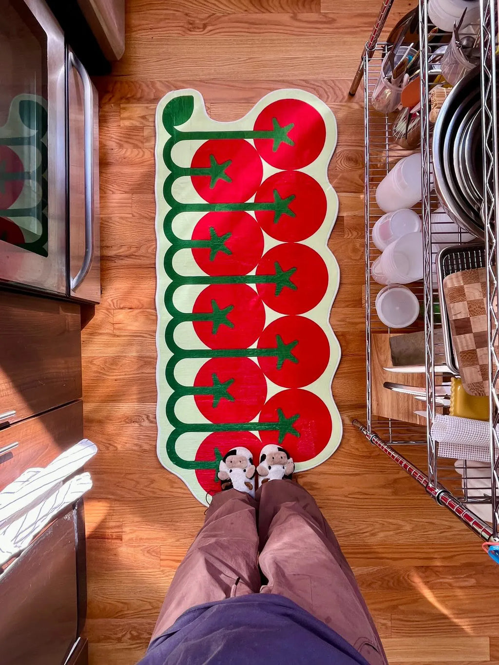 Tomato-cluster kitchen rug in bright red and green on hardwood floor, top-down view with feet in cow slippers.