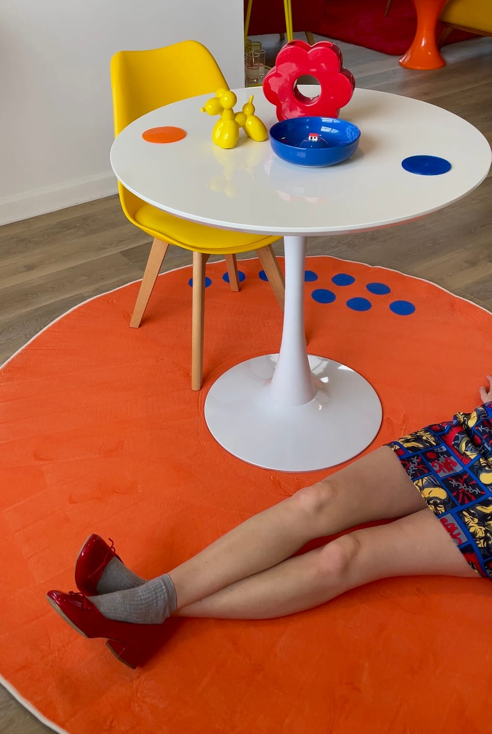 White round table with colorful toys on a wooden floor, person sitting on an orange rug.