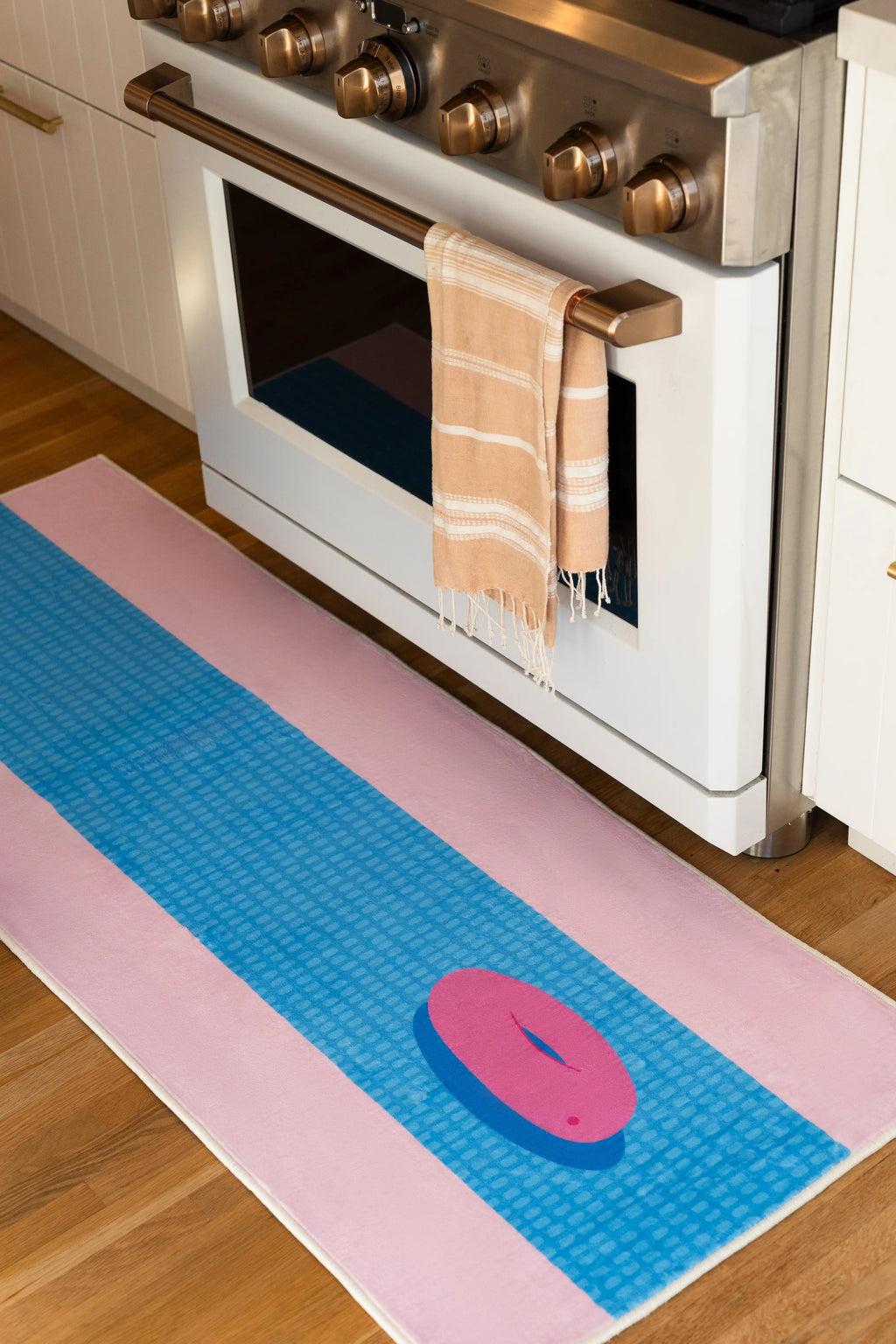 Blue and pink funky pool runner rug beside a white kitchen oven on a light wood floor, with a pink pool float motif