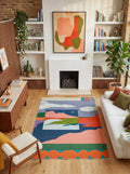 Landscape rug by Sophie Deller styled in a cozy living room with a fireplace, armchair, and wood shelving