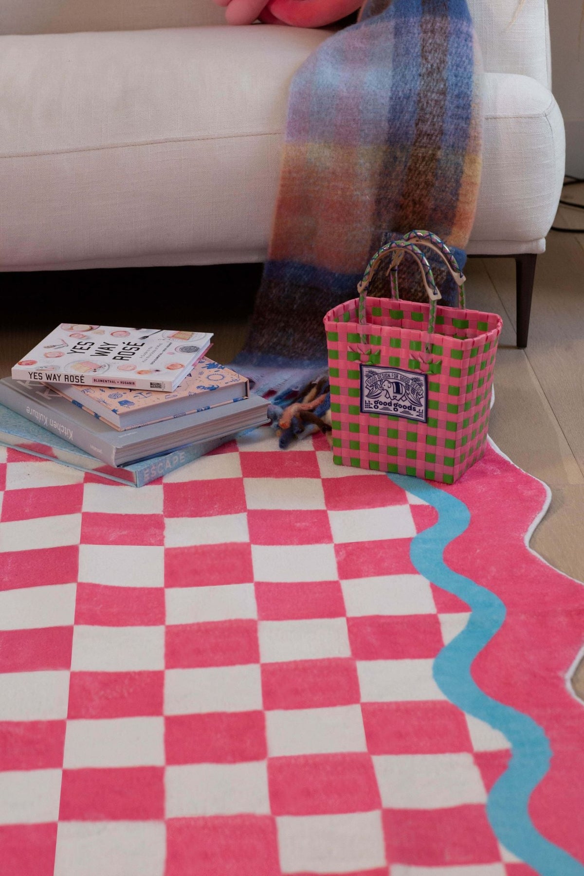 Close-up view of the checkered rug with pink and blue scalloped edges, books and a woven basket adding cozy detail.