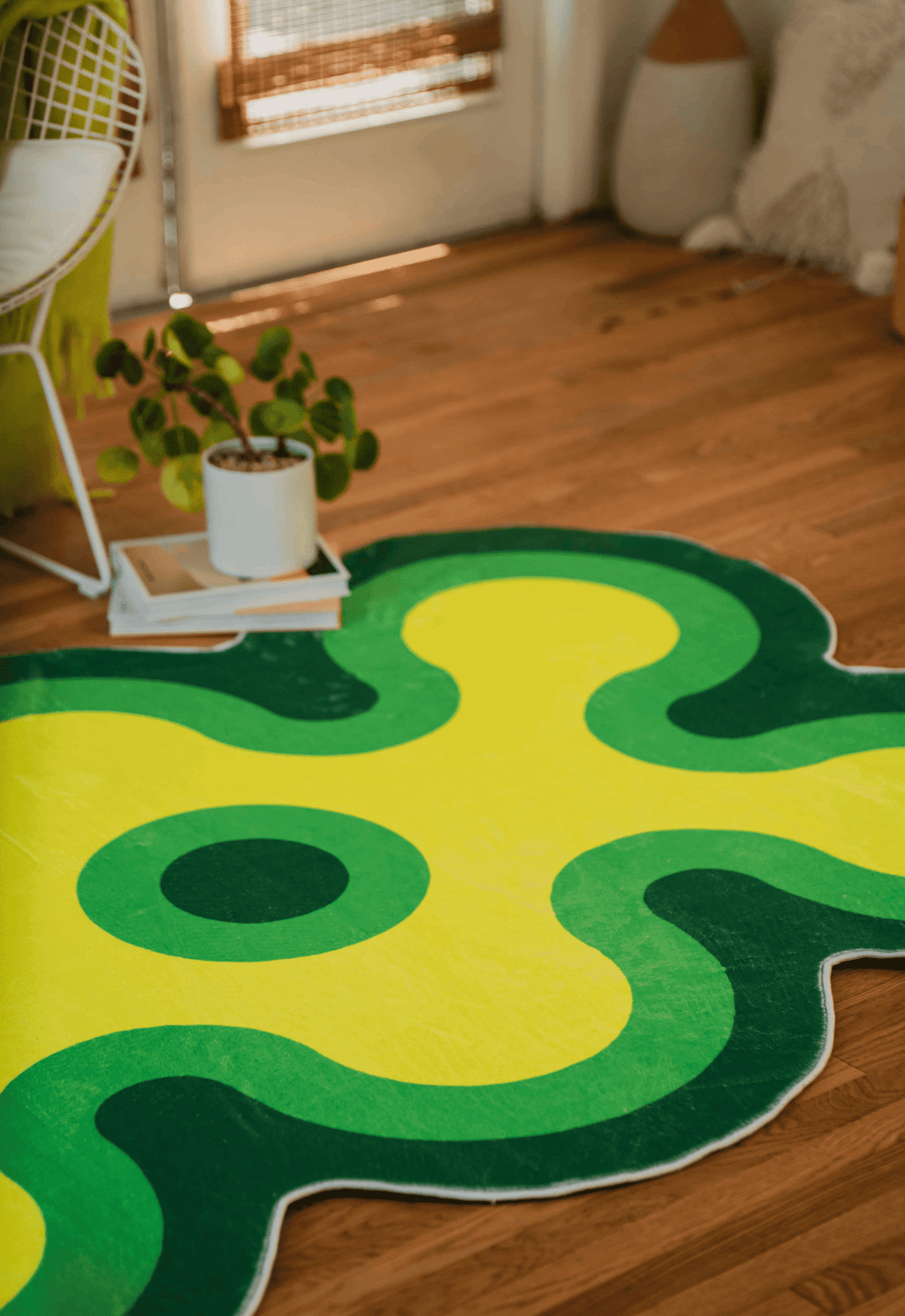 Side view of the green and yellow abstract rug in a sunlit room, next to a potted plant and door.