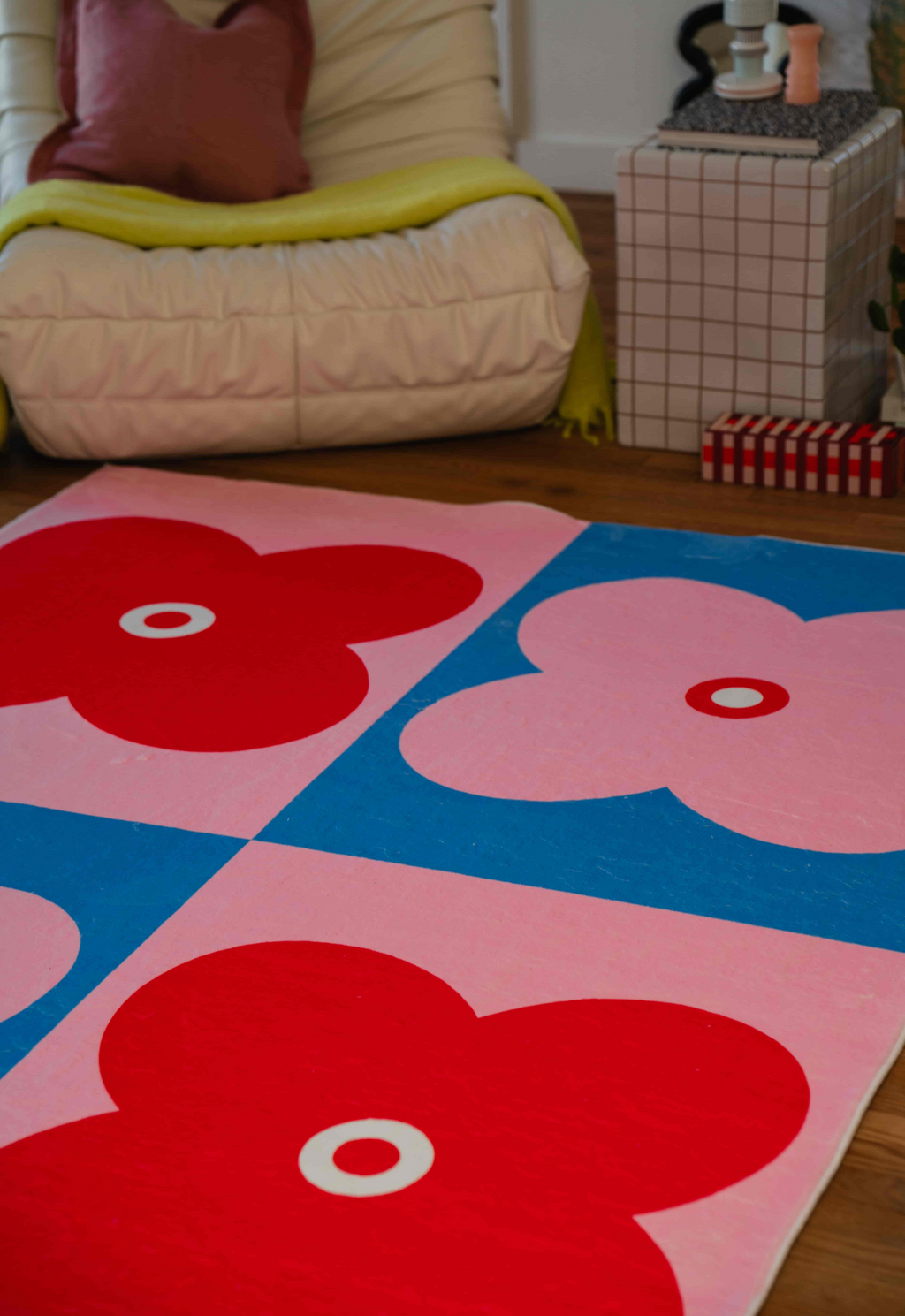 Close-up of red and pink four-leaf flower rug pattern near a cream armchair and grid side table.