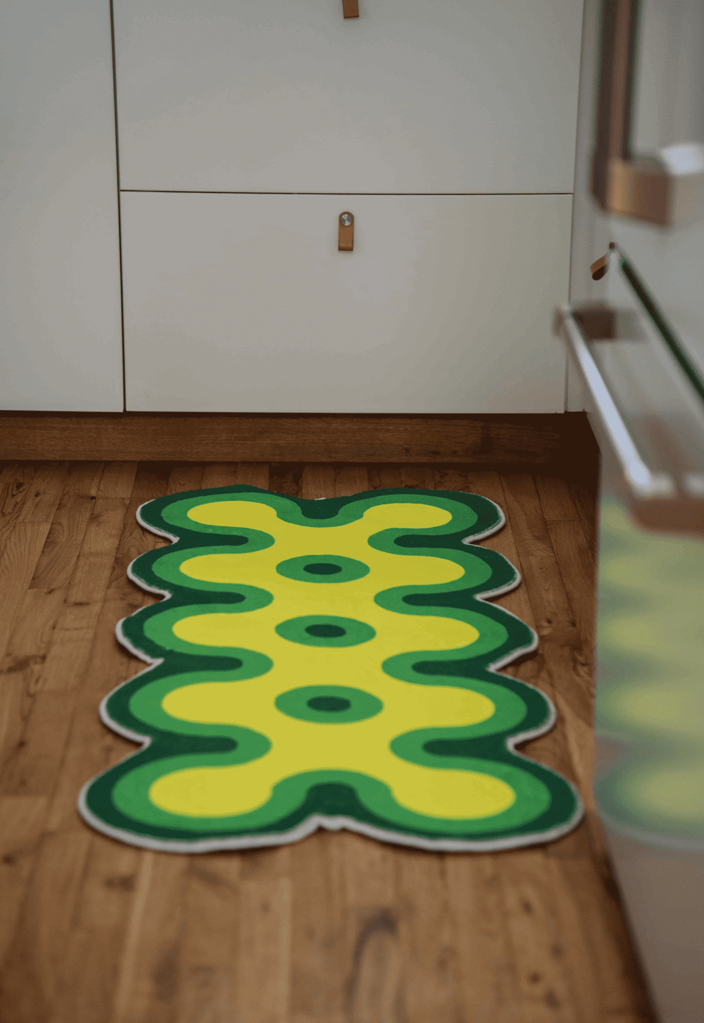 Irregular coral design runner in green and yellow laid on wood floor next to lower white drawers.