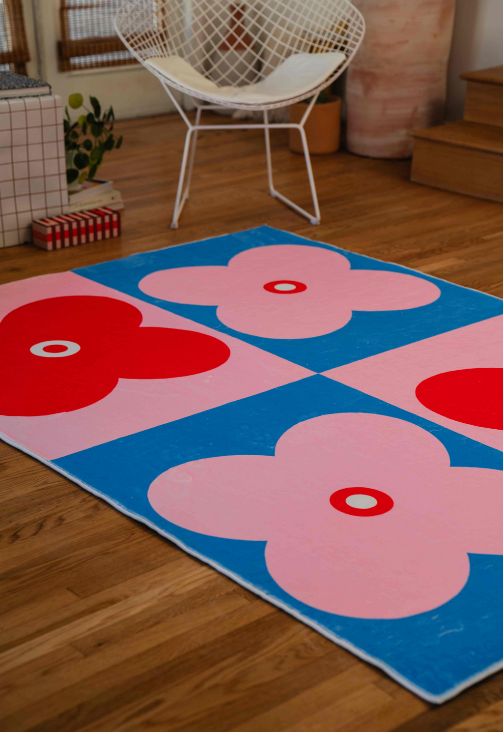 Pastel floral rug with pink and red flowers beside a white wire chair and wooden steps in a bright room.