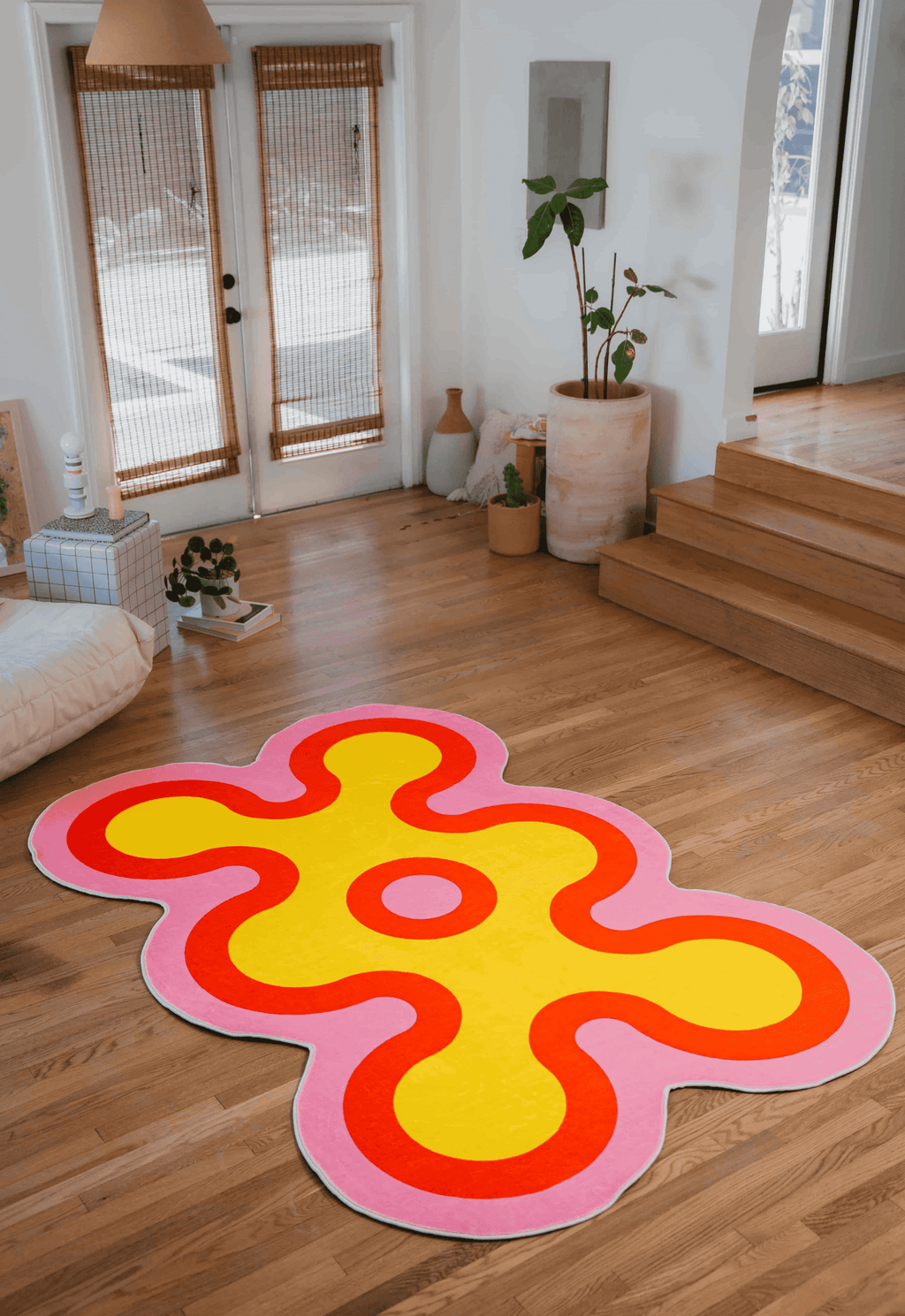 Yellow abstract rug with pink and red borders placed near patio doors and indoor plants in a bright living room.