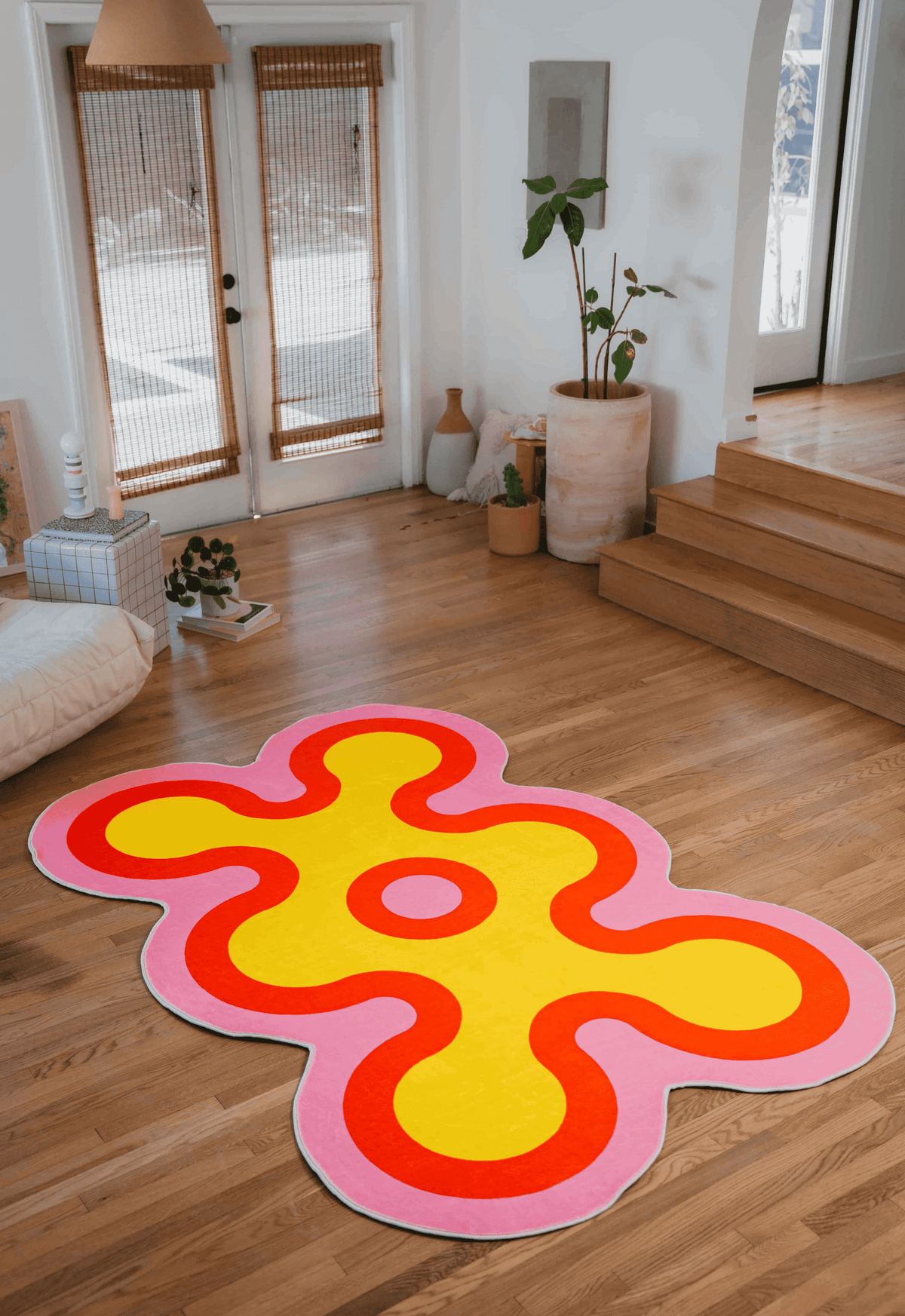 Yellow abstract rug with pink and red borders placed near patio doors and indoor plants in a bright living room.