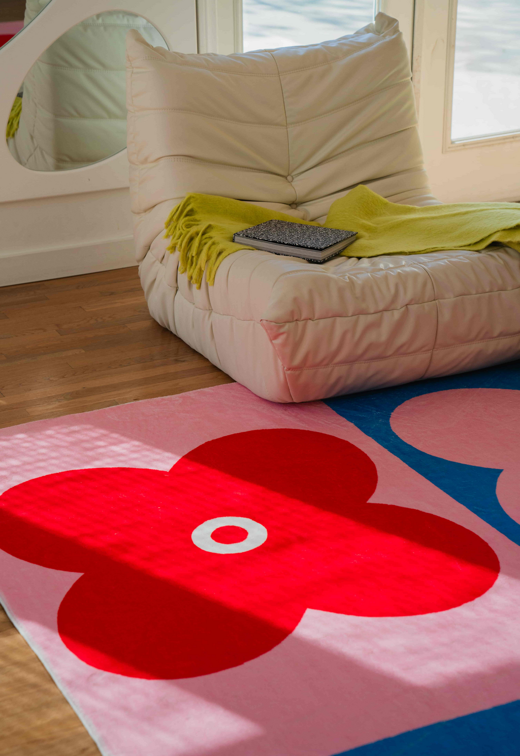 Bright red and pink clover rug beside a cream lounge chair and soft green throw in natural sunlight.