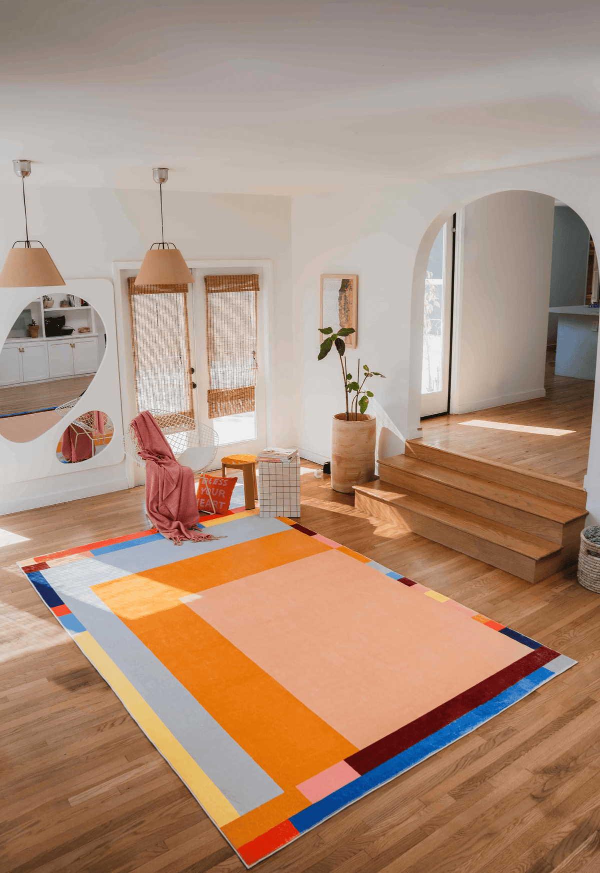 Modern Geometric Print Rug in a sunlit room with soft pink throw, grid ottoman, and orange accent pillow on warm wooden floors.