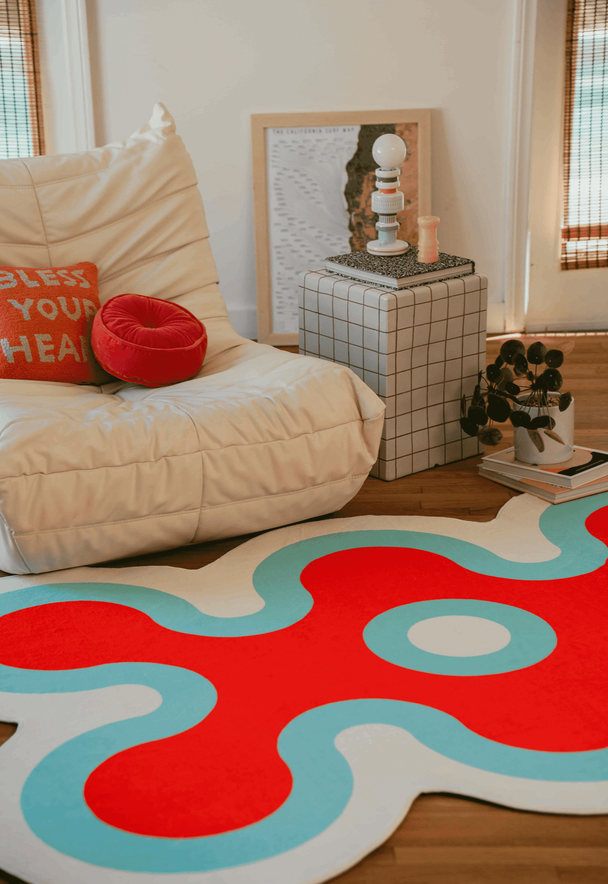 Red and light blue coral-shaped rug beside white lounge chair with red cushion, near full-length windows.