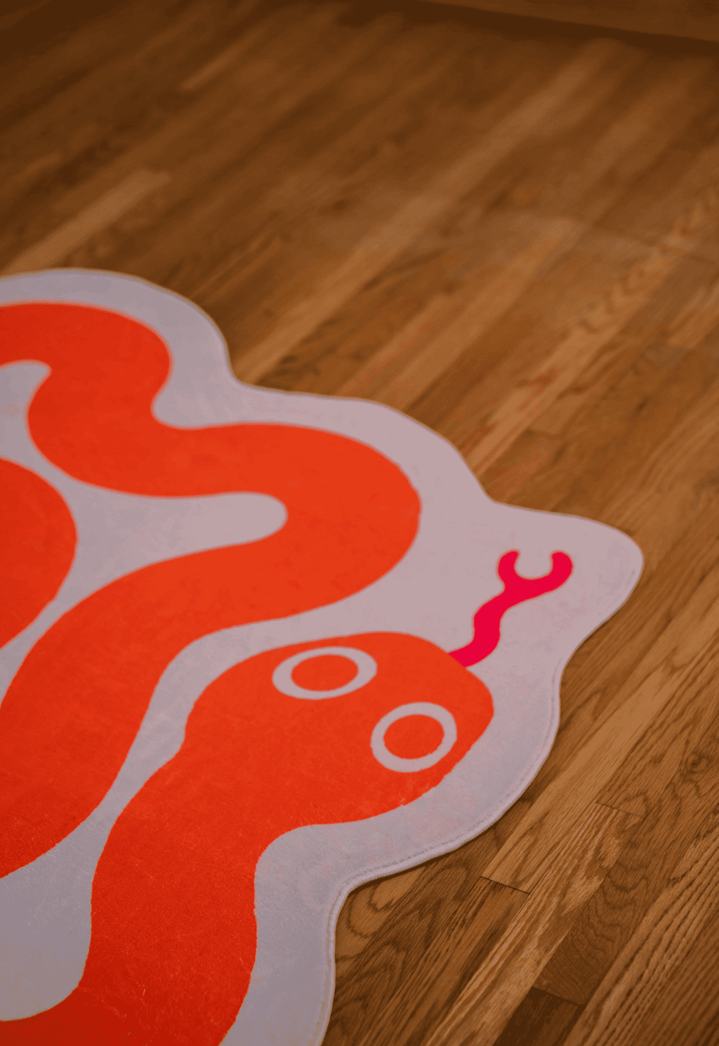 Detail of the snake’s head and tongue on the orange snake rug placed on warm wood floor.