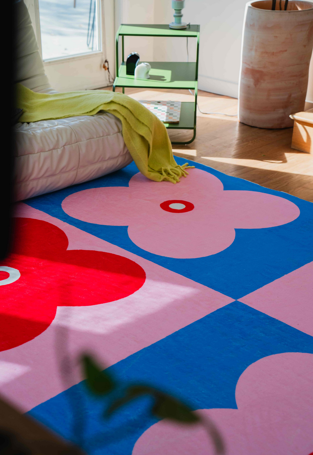 A pink-and-red version of the clover rug styled in a bright room with wooden floors and minimal modern decor.