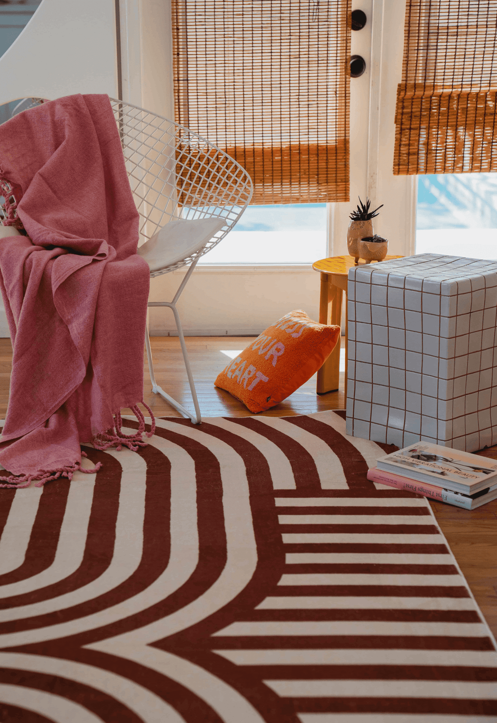Close-up of the striped rug with a white metal chair, pink throw, and an orange pillow nearby.