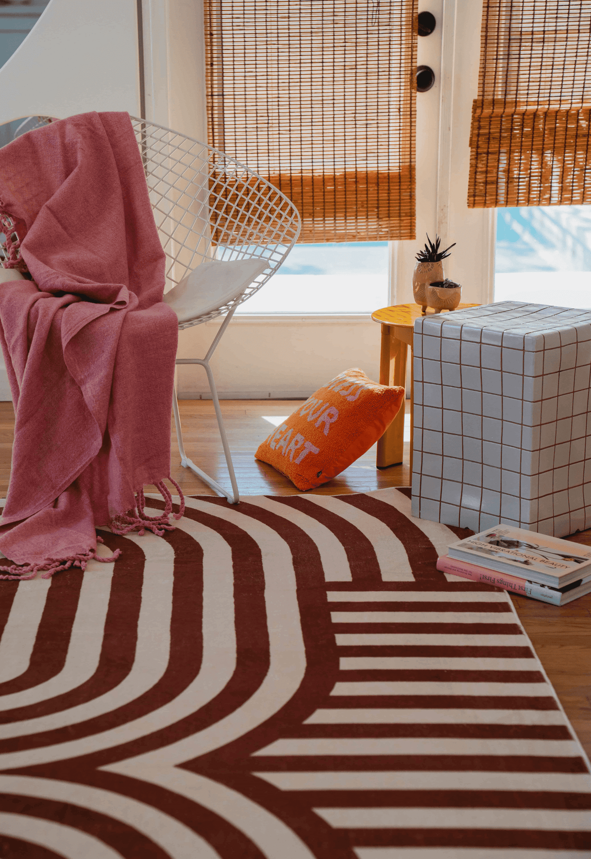 Close-up of the striped rug with a white metal chair, pink throw, and an orange pillow nearby.