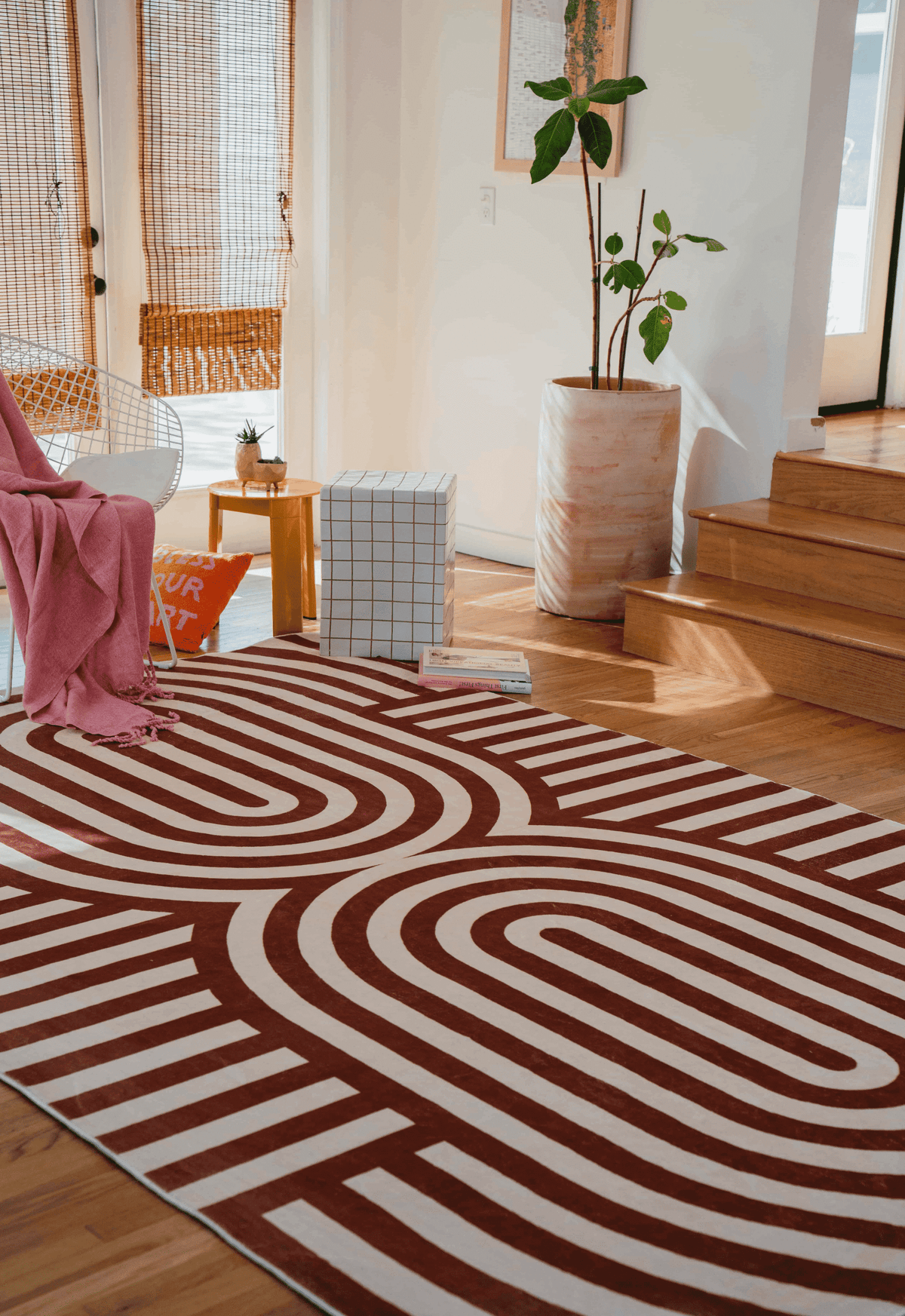 The striped rug placed near white walls, wooden steps, and decor items like a round yellow side table and books on the floor.