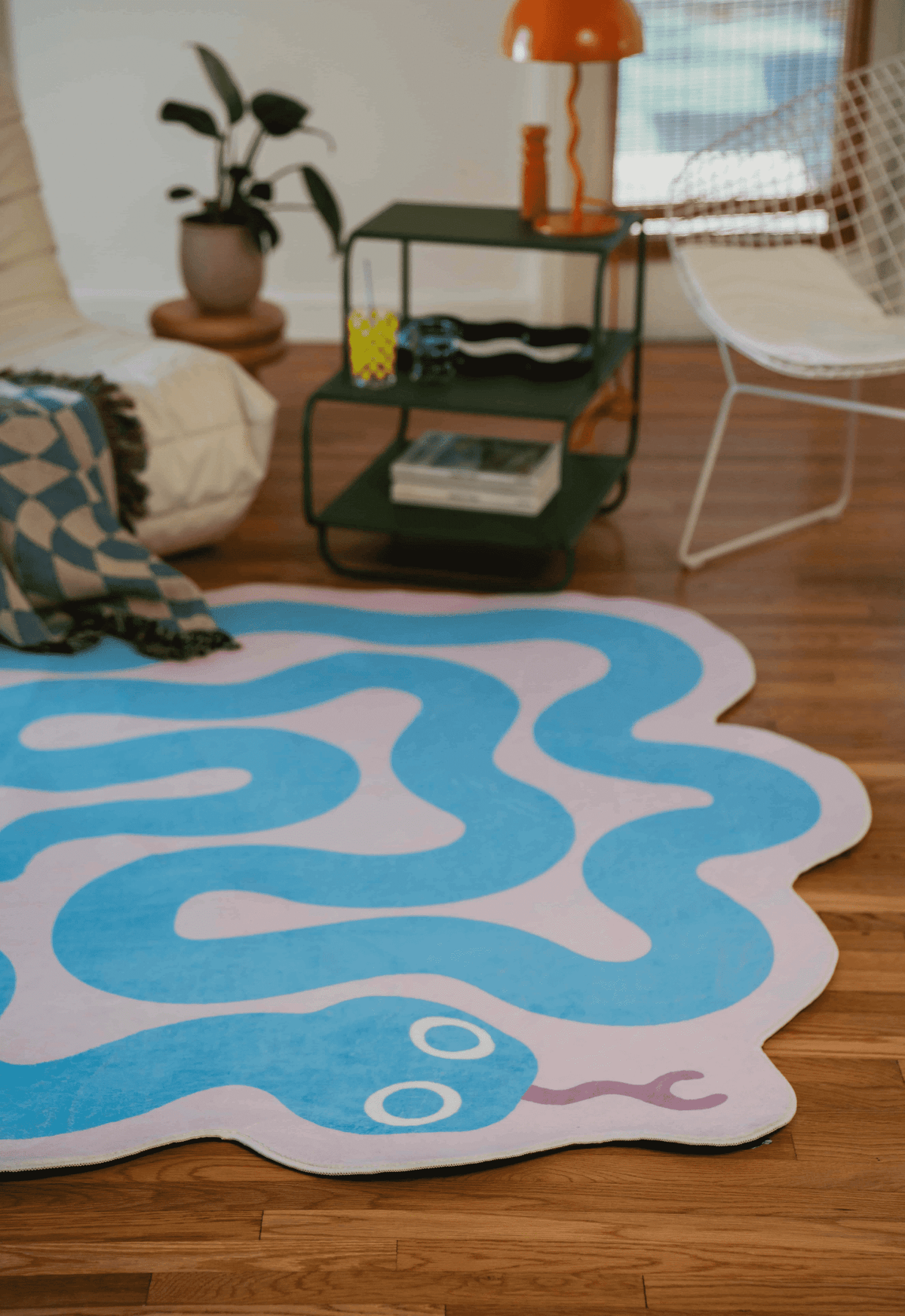 Blue snake rug in a bright room with wooden floors, next to a lounge chair, green shelf, and orange table lamp.