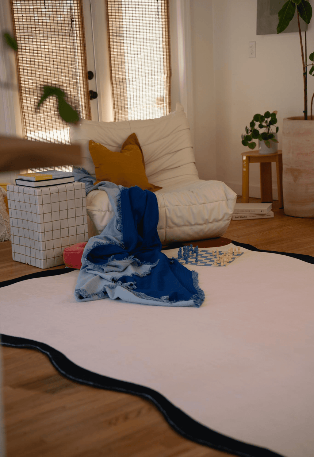 A cozy living room setup featuring the ivory rug with wavy edges, a white lounge chair with mustard pillow, and a blue throw draped over the corner.