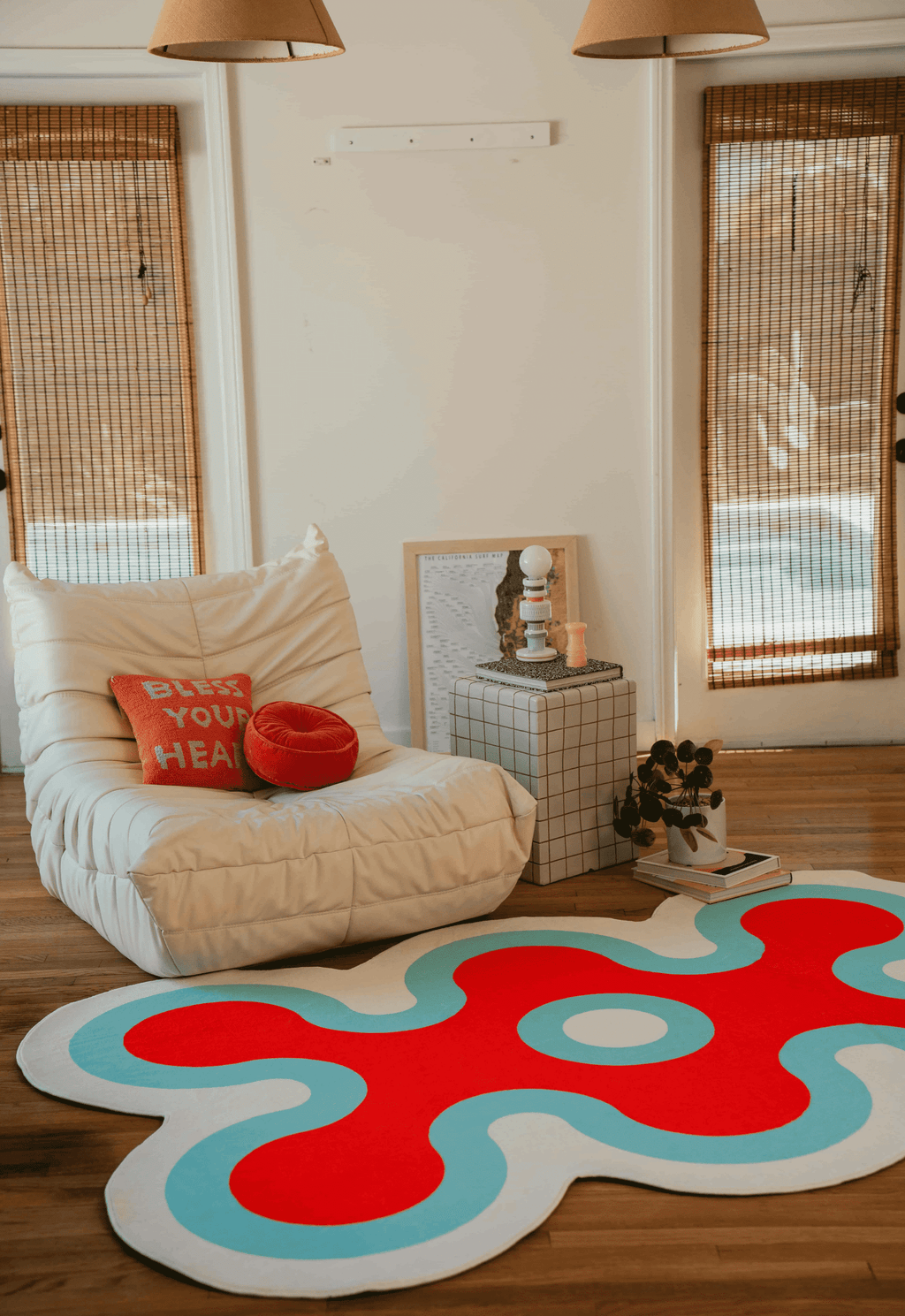 Coral rug in red and blue placed in front of low cream chair, framed by two tall windows with bamboo blinds.