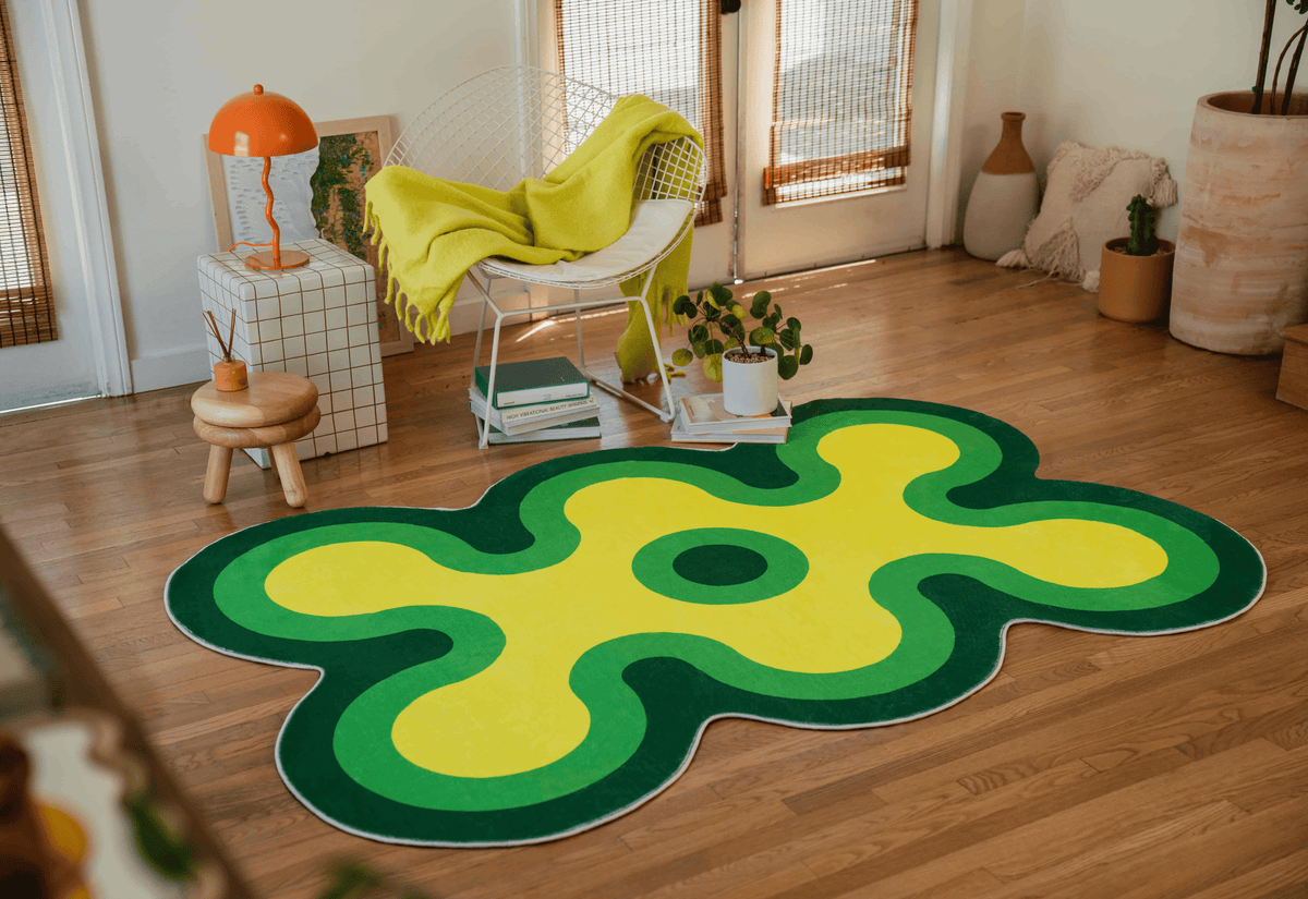 Wide shot of the green and yellow wavy rug in a cozy space with a white chair, books, and a terracotta planter.