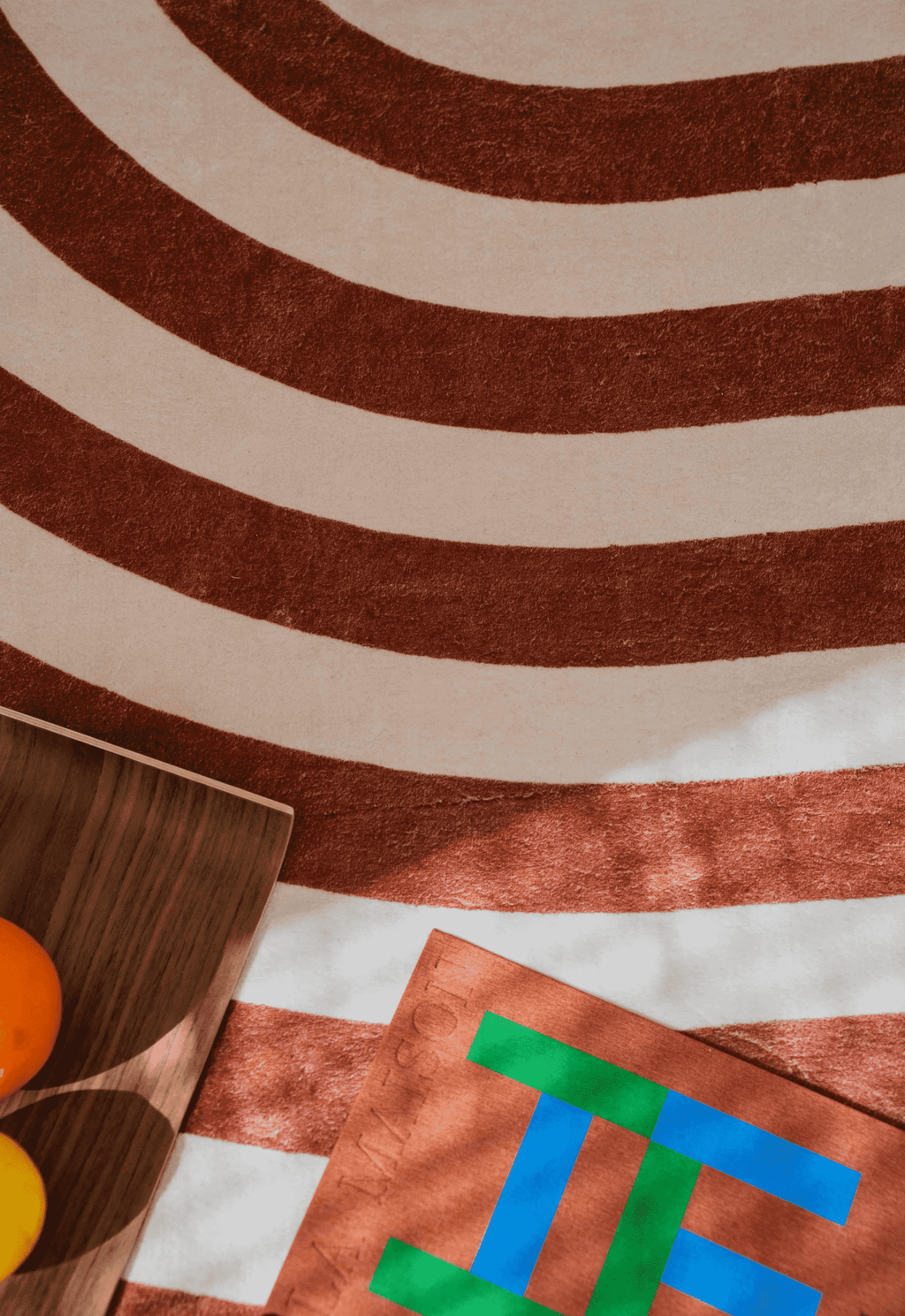 Detail shot of the rug’s plush texture with curved brown stripes, styled with a wooden tray of oranges and a bold art book.
