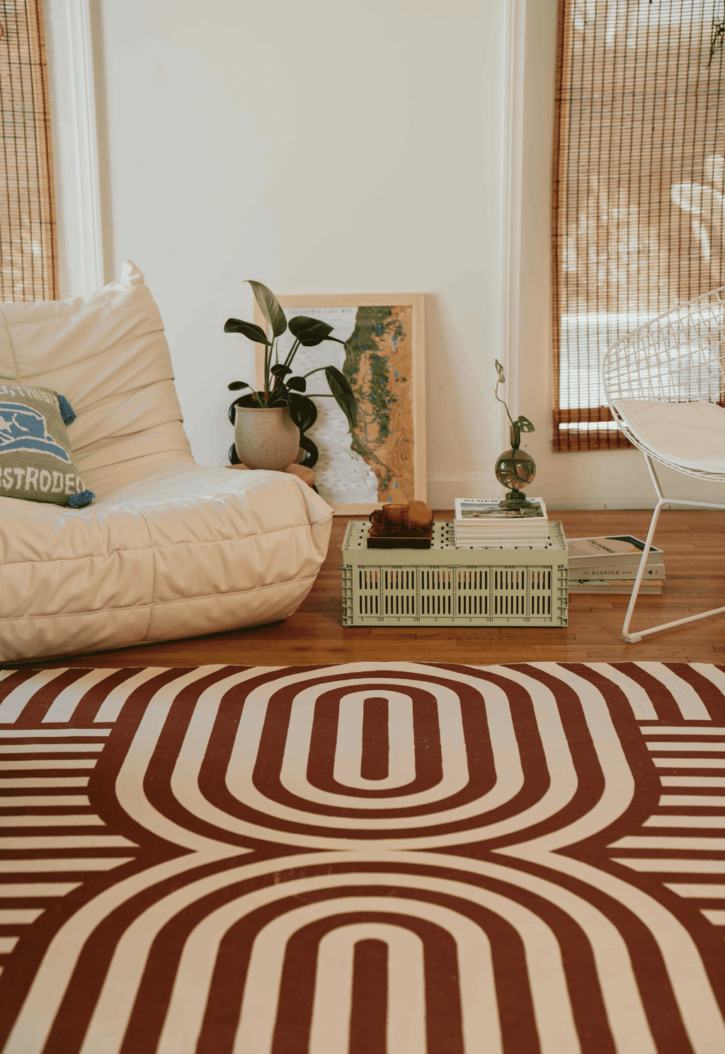 Detail of the rug’s bold curved lines next to a white grid cube table, wire chair draped with a pink throw, and orange accent pillow.