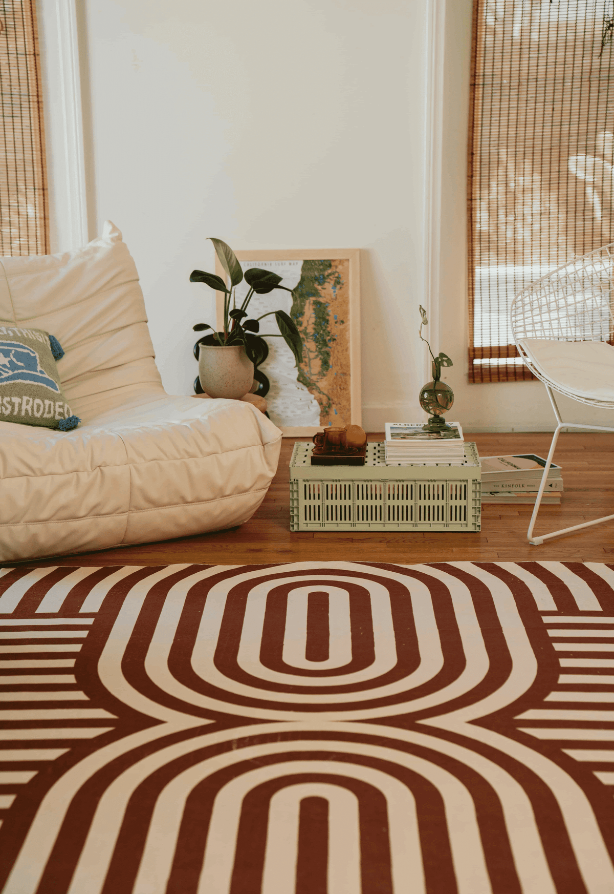 Detail of the rug’s bold curved lines next to a white grid cube table, wire chair draped with a pink throw, and orange accent pillow.
