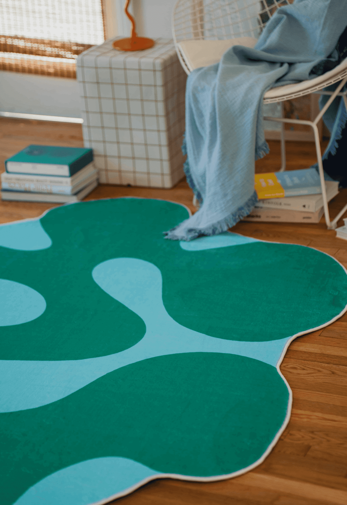 Close-up of green moss rug next to white chair with blue throw and stacked books on a wooden floor.