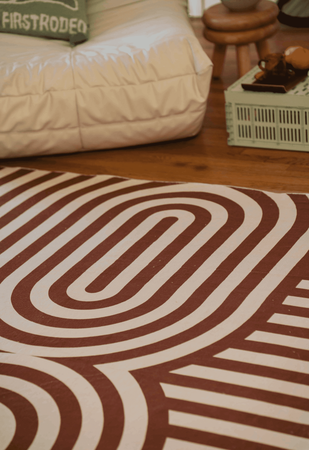 Close-up of the retro-style rug’s oval stripe pattern next to a white chair and mint green crate used as a coffee table.