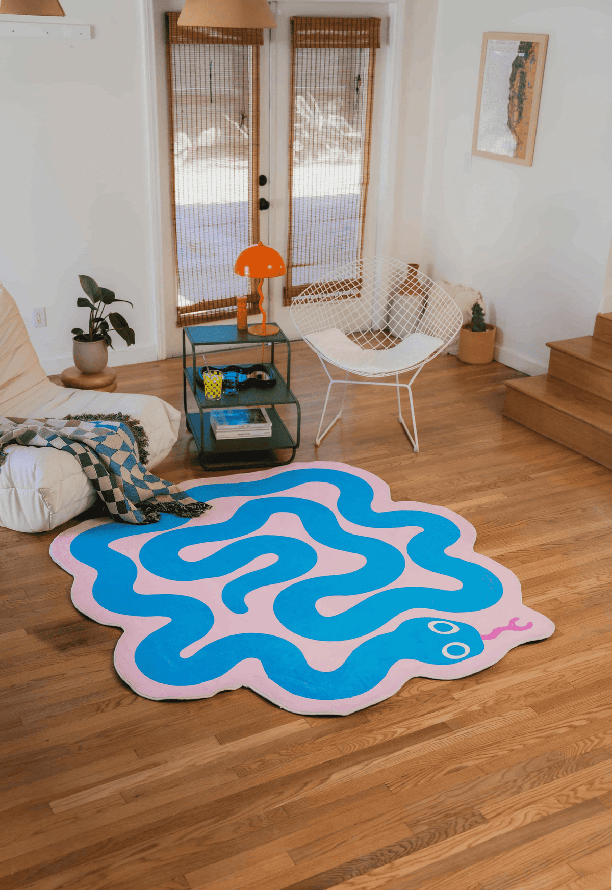 Pink and blue snake rug laid out on wood floor next to a cozy seat draped with a checkered throw blanket.