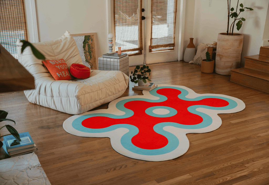 Close-up of the coral rug in red, white, and blue placed beside a white lounge chair with red and orange cushions.