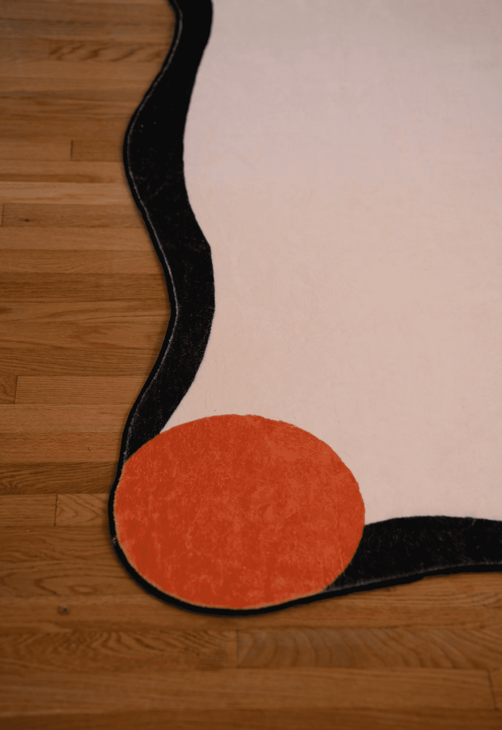 Detail of the irregular rug's red corner dot and wavy black border on hardwood floor.